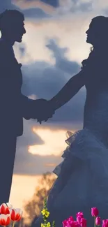 Romantic silhouette of a couple against a sunset sky with flowers below.