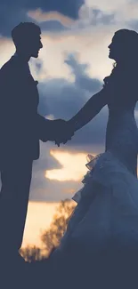 Silhouetted couple holding hands at sunset with dramatic sky.