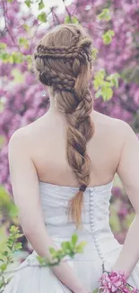 A woman in white stands in front of pink blossoms with a braided hairstyle.