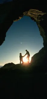 Silhouette of couple under cliff arch during sunset.