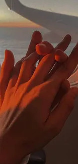 Hands holding by plane window with sunset glow.