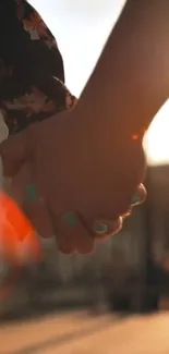 Two hands holding at sunset with warm orange glow.