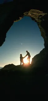 Silhouette of a couple at sunset through a natural rock arch with an ocean view.