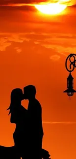 Silhouette of a couple kissing at sunset under orange sky.