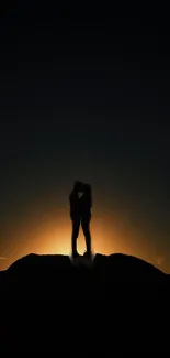 Silhouette of a couple embracing at sunset on a hilltop against a dark sky.