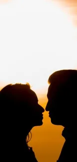 Silhouette of a couple kissing at sunset with a warm orange glow.