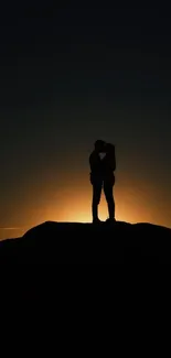 Couple silhouette against a sunset background on a hill.