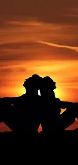 Silhouetted couple against orange sunset backdrop.