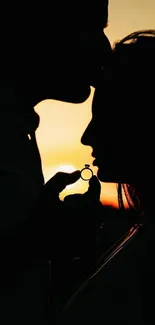 Silhouette of couple at sunset, holding a ring, creating a romantic ambiance.