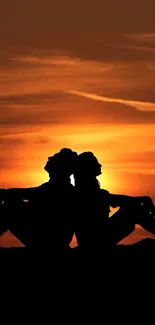 Silhouette of a couple sitting back-to-back against a vivid orange sunset sky.