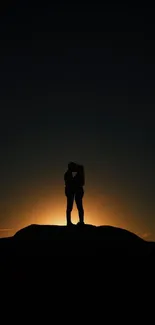 Silhouette of a couple embracing at sunset on a rocky hill.