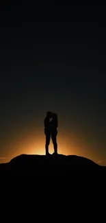 Silhouette of a couple embracing at sunset with a glowing horizon.