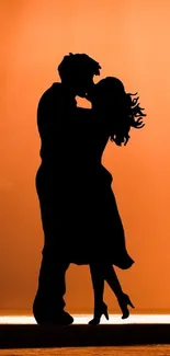 Silhouette of a couple embracing at sunset with an orange sky.