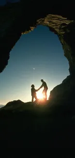 Silhouetted couple in a rock arch at sunset on a beach.