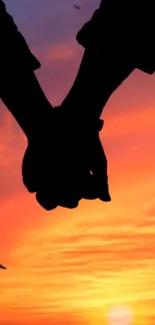 Silhouette of a couple holding hands against an orange sunset sky.