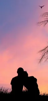 Silhouette of a couple against a pink sunset sky with a bird flying above.