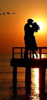 Silhouette of couple kissing at sunset on a pier with flock of birds flying nearby.