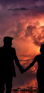 Silhouette of a couple holding hands against a dramatic sunset sky.