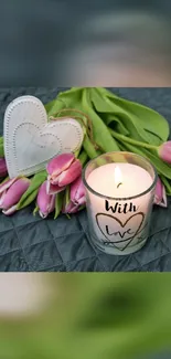 Bright candle with tulips and heart ornaments on a dark quilted surface.