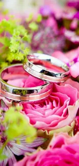 Silver wedding rings on pink roses with vibrant floral background.