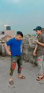 Two people in casual attire on a rooftop with a city skyline.