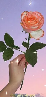 Hand holding a rose against a pastel moonlit sky wallpaper.