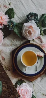 Delicate tea cup surrounded by pink roses and greenery.