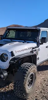 Off-road Jeep Rubicon on rocky terrain with mountain backdrop.