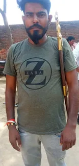 Man in rural attire holding a stick, set outdoors.