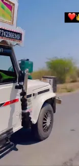 White SUV driving on a rural road under a clear sky.