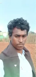 Young man takes a selfie in a rural area with heart and sparkle effects under blue sky.