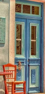 Rustic blue door with red chair and table in sunlit setting.