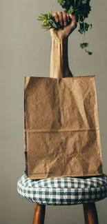 Hand holding herbs over a brown bag on a stool.