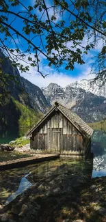 Rustic cabin by a serene mountain lake with snowy peaks in the background.