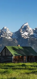 Rustic cabin with green roof and mountain peaks in the background.