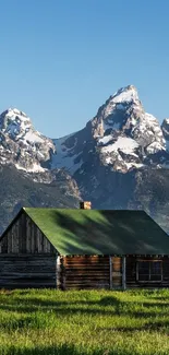 Rustic cabin with snow-capped mountain backdrop and green field.