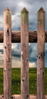 Rustic wooden fence with stormy sky and grassy field.