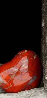 Heart-shaped red stone on rustic wood surface.