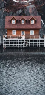 Rustic wooden house by a tranquil cliffside lake.