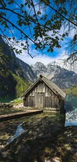 Rustic cabin beside a reflective mountain lake under a clear blue sky.
