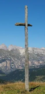 Wooden cross on a mountainside with clear blue sky and distant peaks.