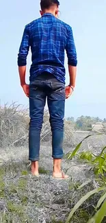 Man standing barefoot in field with blue shirt in a rural setting.