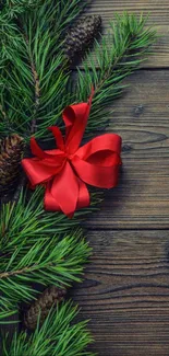 Rustic holiday wallpaper with pine branch and red bow on wood.