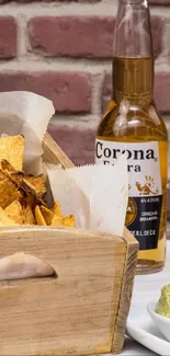 Rustic table setup with chips, guacamole, salsa, and drink on brick wall background.