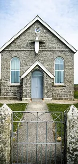 A rustic stone church in a peaceful countryside landscape with a cloudy sky.