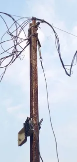 Rustic utility pole with tangled wires against a blue sky.