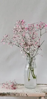 Delicate pink wildflowers in a rustic vase on wooden bench.