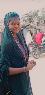 Woman in traditional attire in a rural village setting with rustic background.