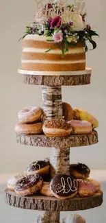 Rustic wedding cake with floral decor and donuts on a wooden stand.