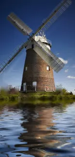 Rustic windmill reflected in tranquil water under a blue sky.